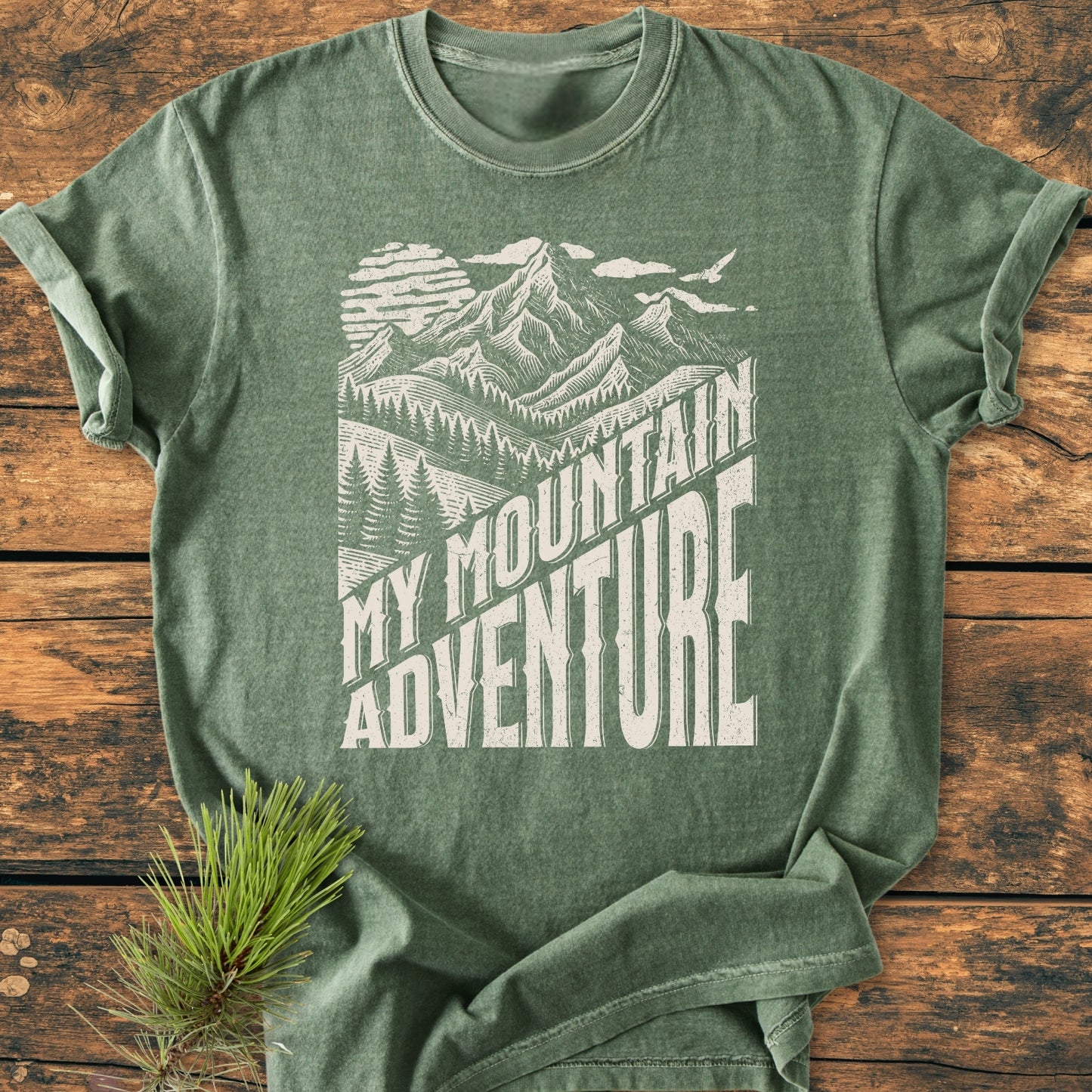My Mountain Adventure - Vintage Wash Tee features a heather-green color with a screen-printed mountain scene and slogan, showcasing its relaxed fit and durable, double-needle stitching on soft-washed cotton.