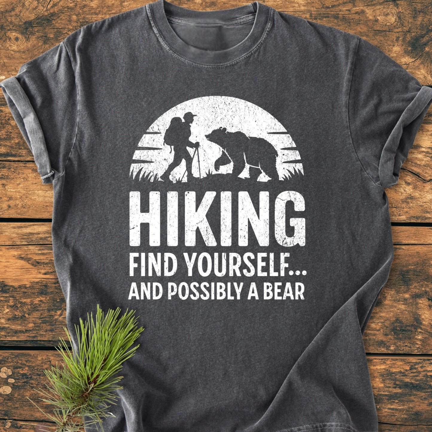 Find Yourself And Possibly A Bear - Vintage Wash Tee displayed on wood, featuring a white half-sun graphic with a hiker and bear, offering a relaxed fit and garment-dyed softness.