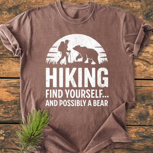 Find Yourself And Possibly A Bear - Vintage Wash Tee features a hiking-themed design with a silhouetted hiker and bear against a stylized sun, printed on a brown Comfort Colors garment-dyed T-shirt.