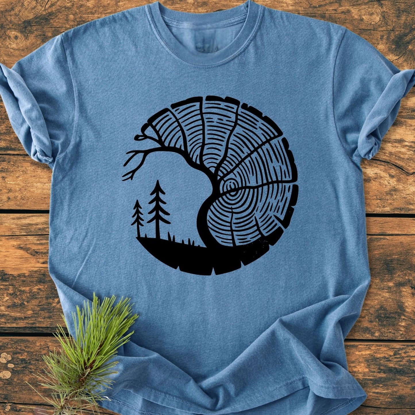 Tree Lover - Vintage Wash Tee: Heather-blue T-shirt featuring a tree-ring and forest scene in black, laid on wood. Made of 100% ring-spun cotton, offering a relaxed fit and durable stitching.