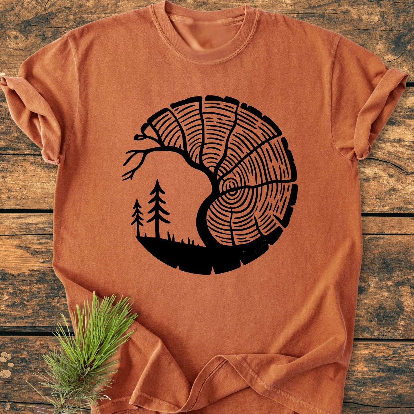 Tree Lover - Vintage Wash Tee, featuring a tree trunk and branch design, is styled flat on weathered wood with a pine bough. Made from cozy, pre-shrunk, 100% ring-spun cotton.