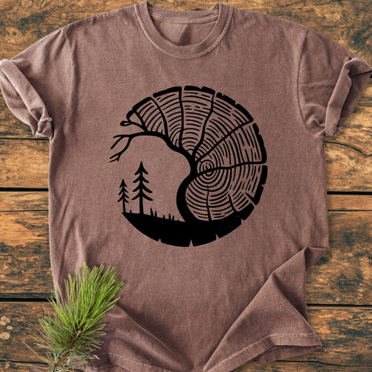 Tree Lover - Vintage Wash Tee: Short-sleeve T-shirt featuring a black screen-printed graphic of tree rings and a landscape silhouette, styled on wood with a pine sprig, highlighting its relaxed fit and durability.