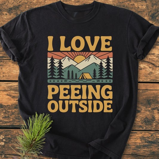 I Love Peeing Outside - Vintage Wash Tee featuring a retro graphic of nature elements on a black T-shirt, laid on a wooden surface, highlighting its relaxed fit and durable, soft-washed fabric.