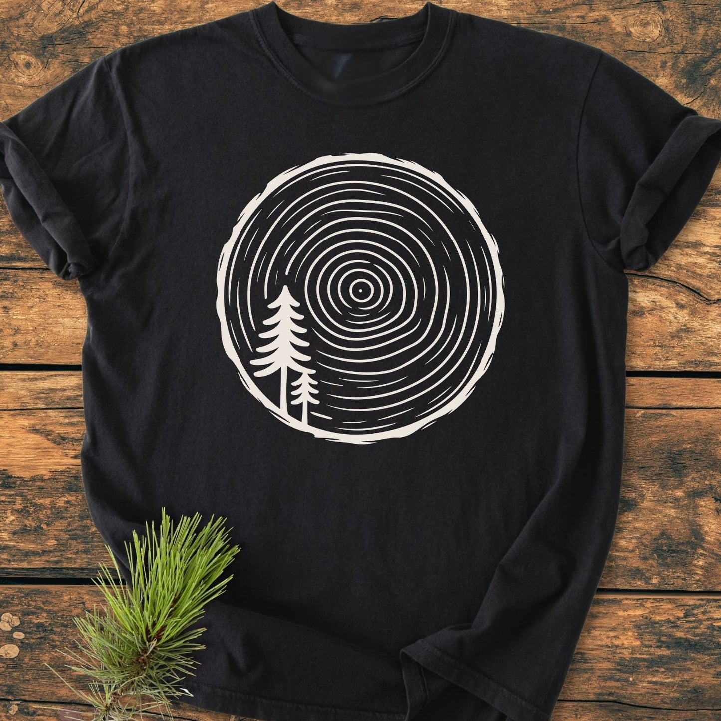 Minimalist Log - Vintage Wash Tee on rustic wood, features a tree-ring graphic with pine silhouettes. Made of 100% ring-spun cotton for comfort and durability, perfect for everyday wear.