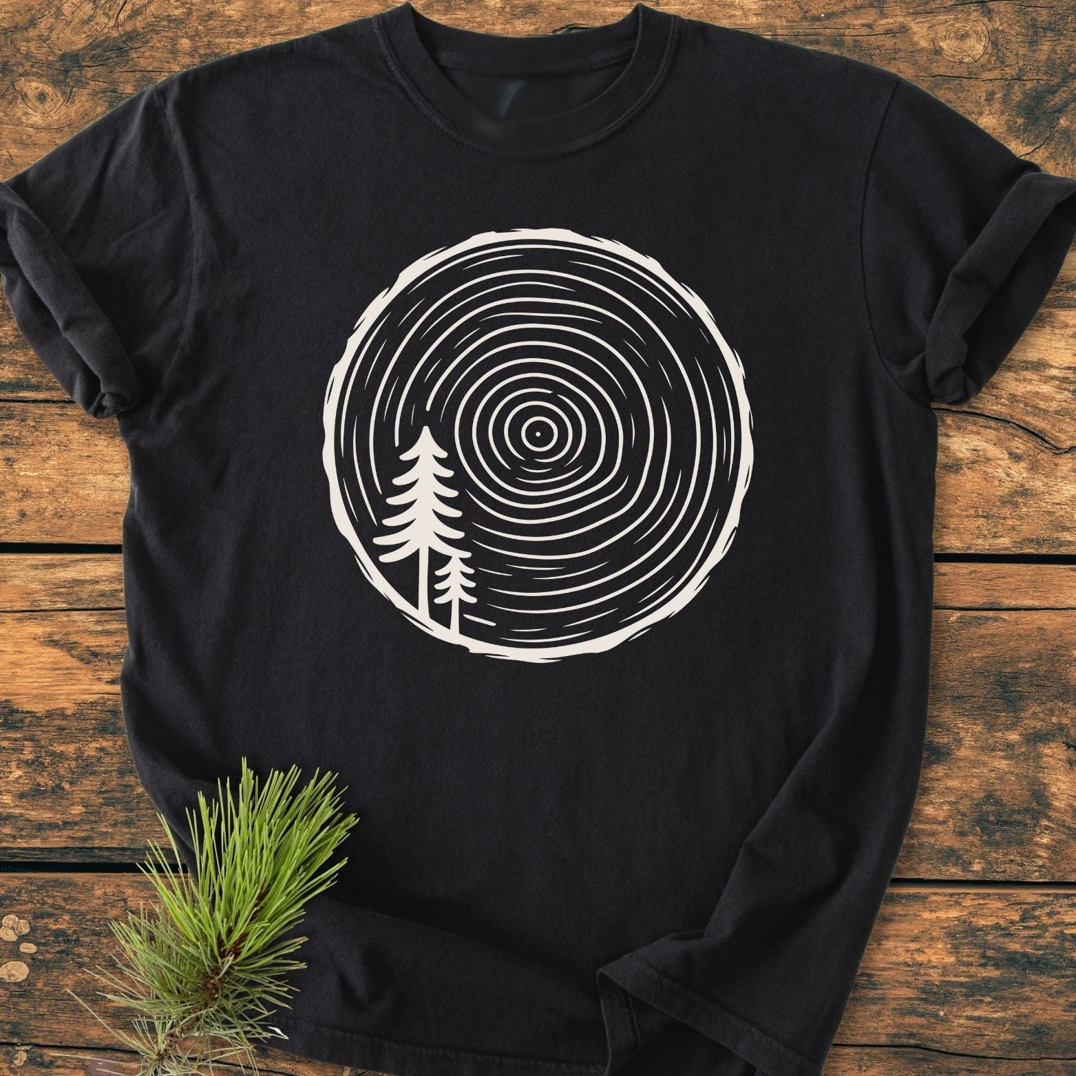 Minimalist Log - Vintage Wash Tee on rustic wood, features a tree-ring graphic with pine silhouettes. Made of 100% ring-spun cotton for comfort and durability, perfect for everyday wear.