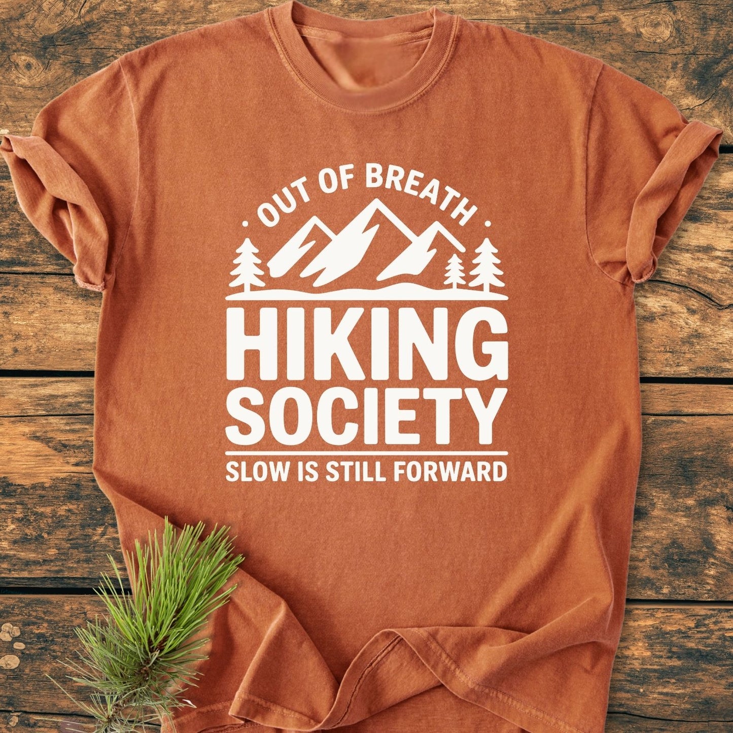 Out Of Breath - Vintage Wash Tee features a mountain design with pine trees, slogans promoting hiking. Laid flat with a pine sprig, it highlights the relaxed, durable, cotton comfort.