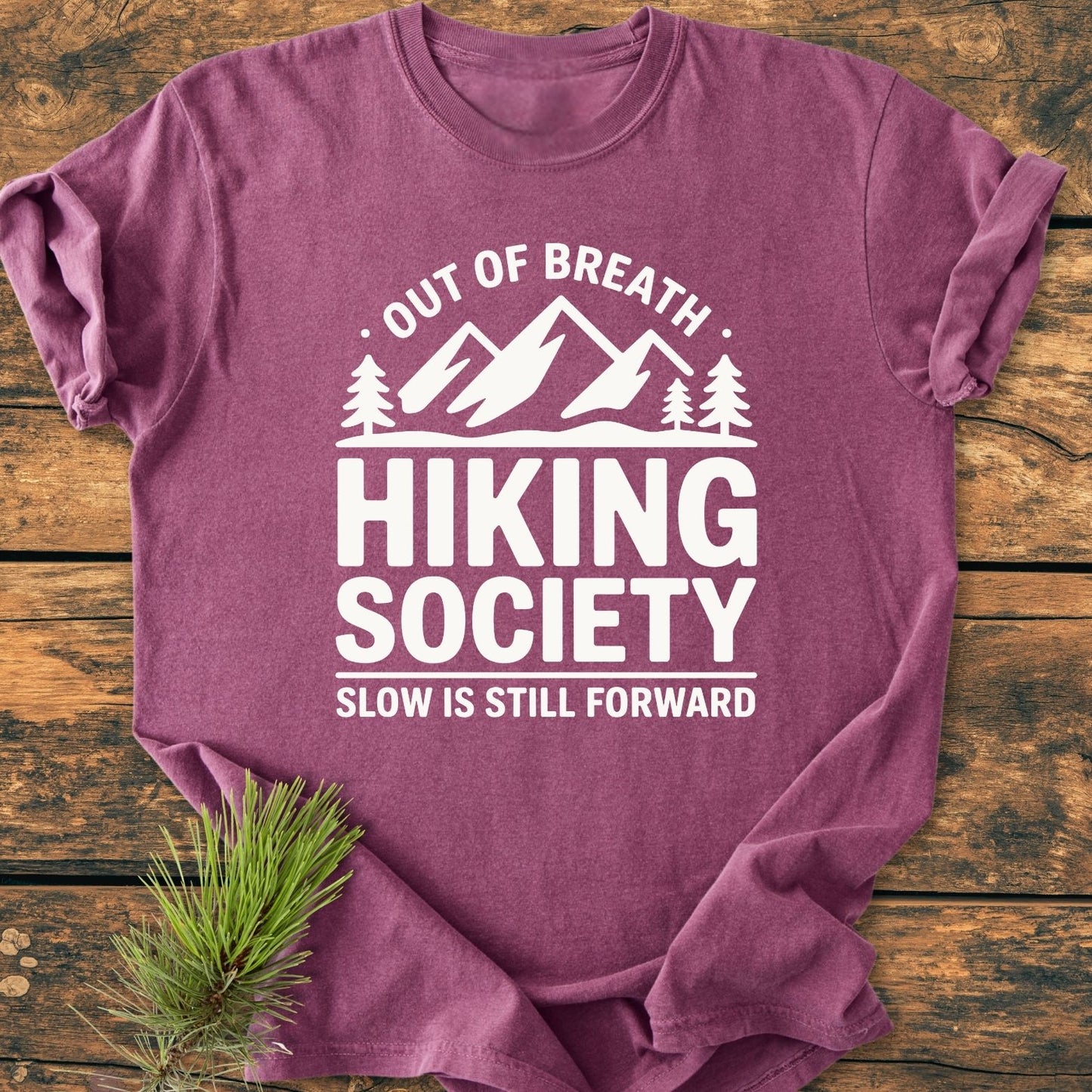 Out Of Breath - Vintage Wash Tee displayed on wood, featuring a mountain-pine graphic and motivational text. Styled with a pine sprig, showcasing the relaxed fit and soft texture of this garment-dyed cotton shirt.