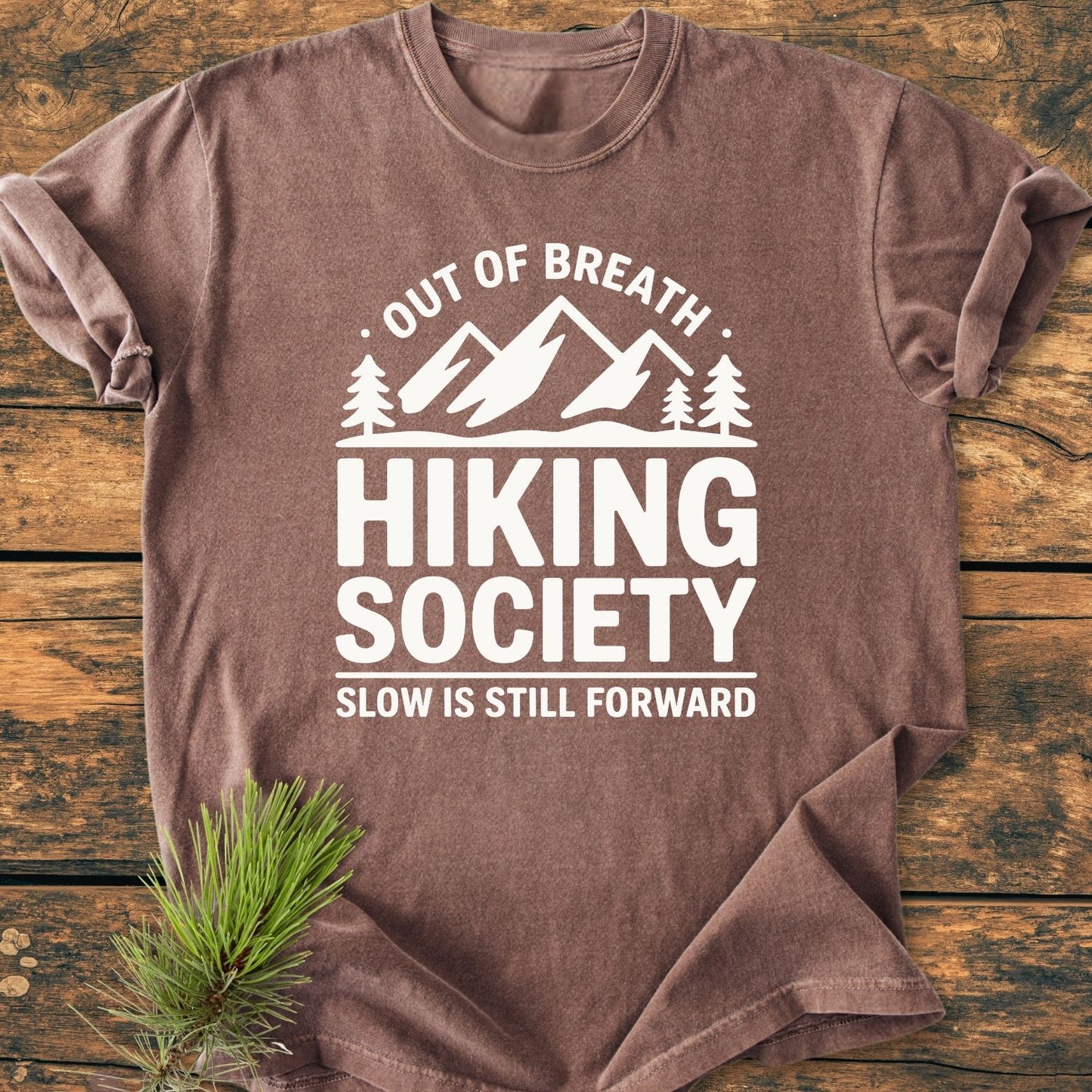 Out Of Breath - Vintage Wash Tee features a mountain graphic with pine trees and motivational text, laid flat on wood. The soft, worn-look design complements its durable, relaxed-fit construction.