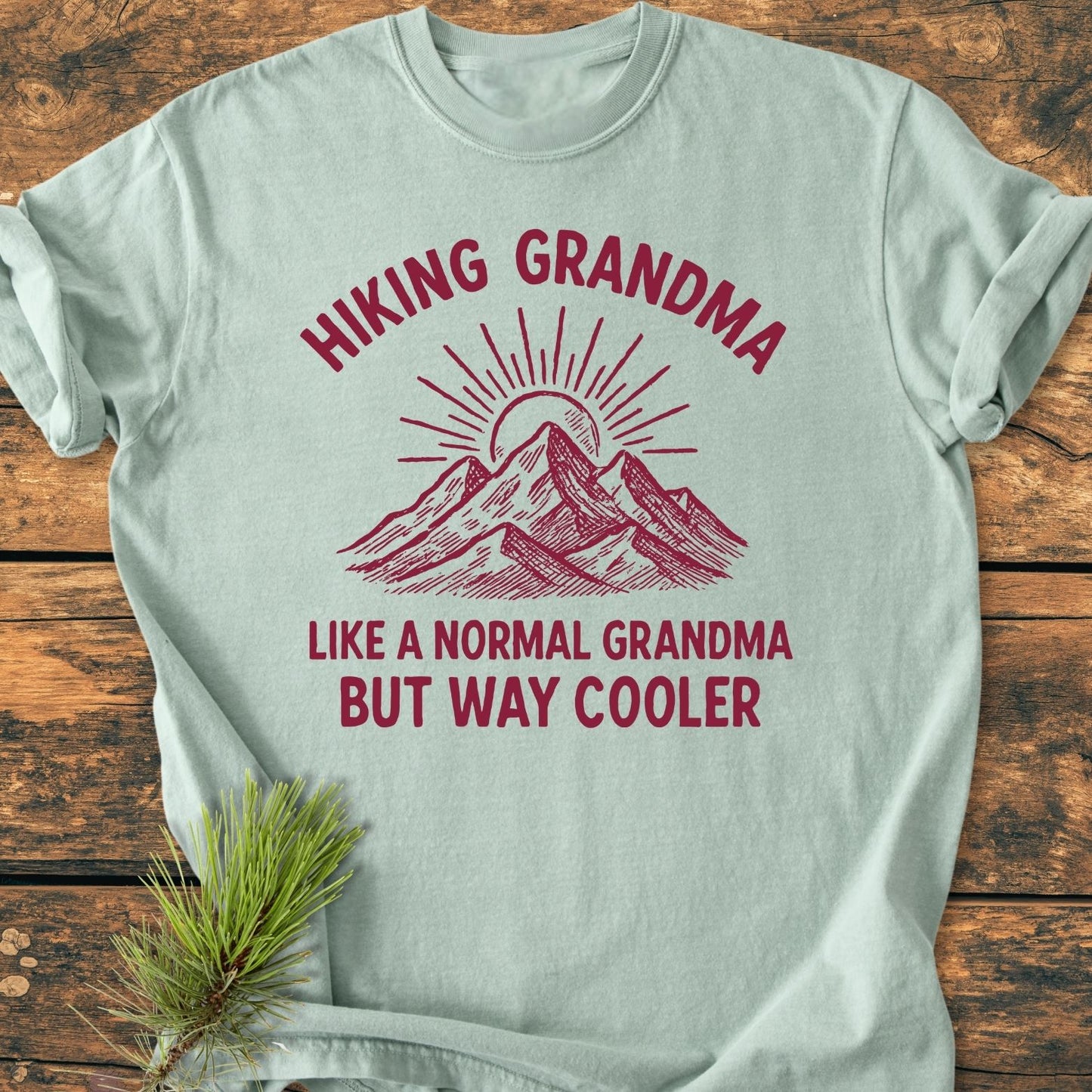 Cool Hiking Grandma Sunrise - Vintage Wash Tee features a stylized mountain and sun design. Laid flat on wood, the tee boasts soft, durable garment-dyed cotton, perfect for relaxed, everyday wear.
