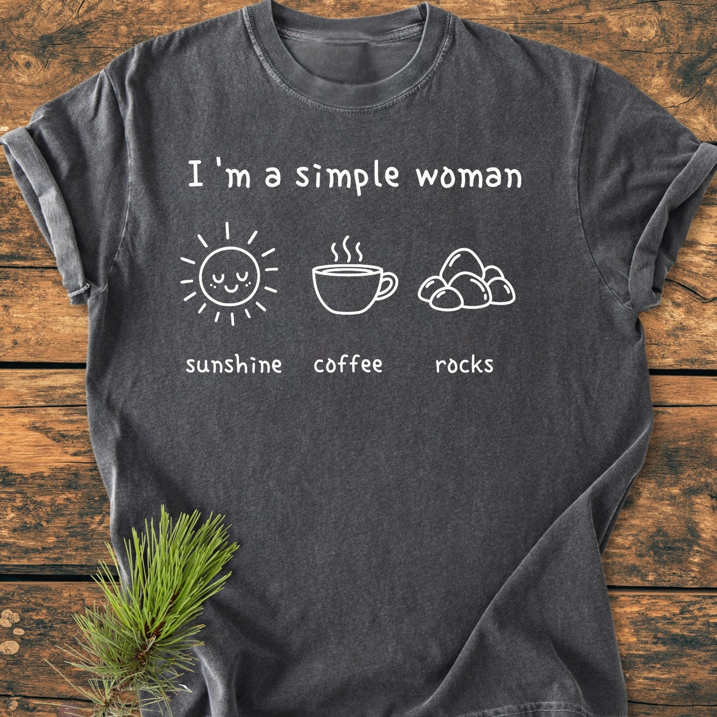 Sunshine, Coffee, Rocks - Vintage Wash Tee in dark-gray cotton, featuring a white print with I'm a simple woman and icons: sunshine, coffee, rocks. Laid on a wooden surface with pine sprig.