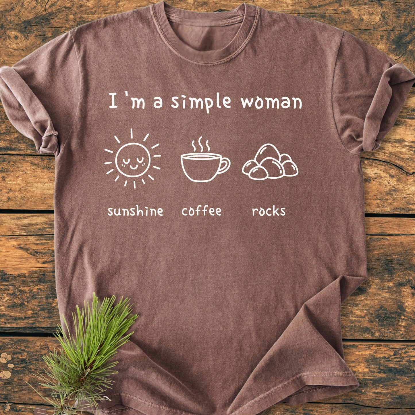 Sunshine, Coffee, Rocks - Vintage Wash Tee displayed on wood features I'm a simple woman with icons: sun, coffee, rocks. Includes a pine sprig, showcasing relaxed, durable, 100% cotton design.
