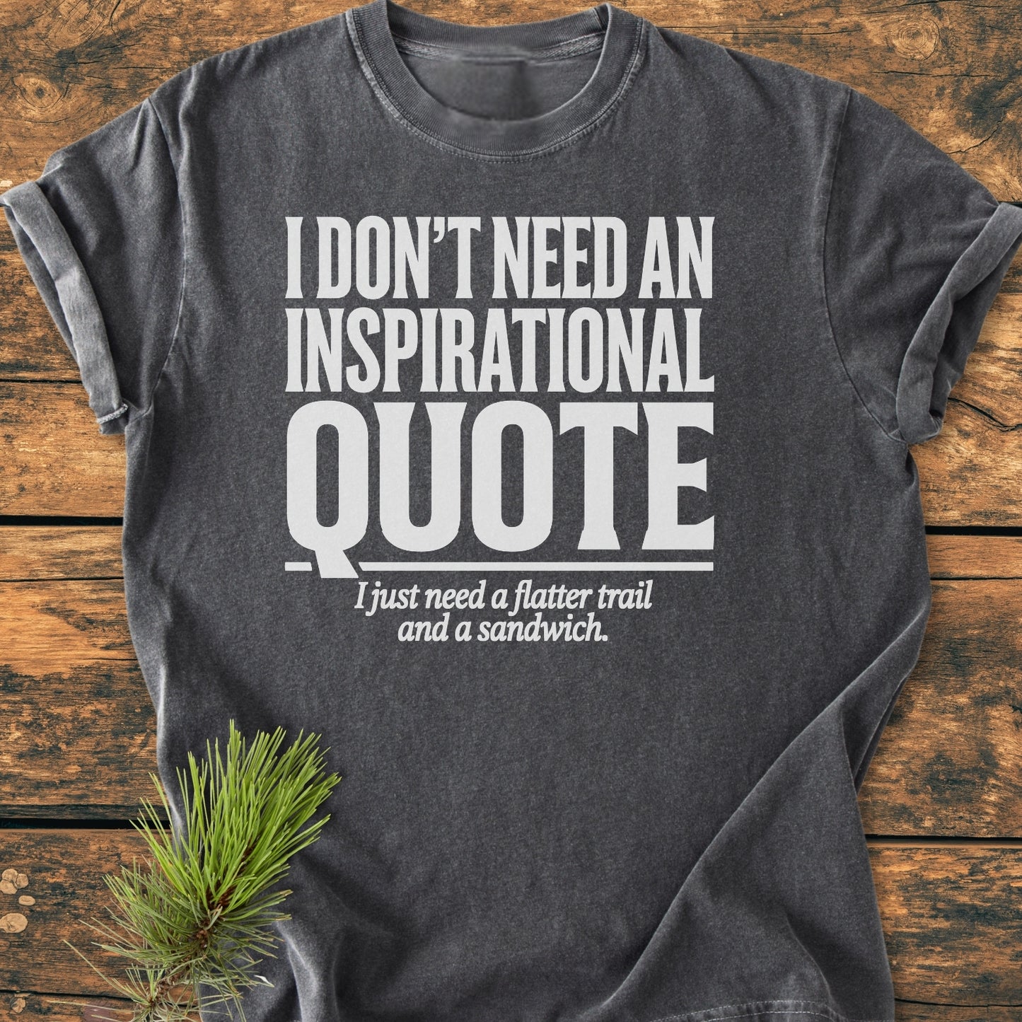 No Inspirational Quote - Vintage Wash Tee in charcoal-gray, featuring a white slogan, laid on wood. A small pine sprig accents the scene, highlighting the shirt's relaxed, cozy appeal.