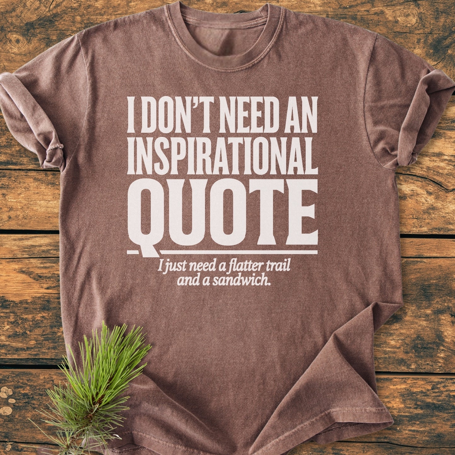 No Inspirational Quote - Vintage Wash Tee displayed on wooden surface, features bold white text humorously stating a preference for simpler pleasures, complemented by a pine needle accent. Relaxed fit, garment-dyed cotton.