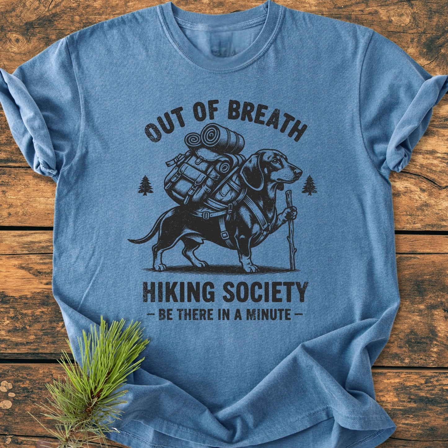 Out Of Breath Dachshund - Vintage Wash Tee features a dachshund with hiking gear, surrounded by pine-tree icons, on a heather-blue Comfort Colors tee, offering a relaxed fit and durable design.