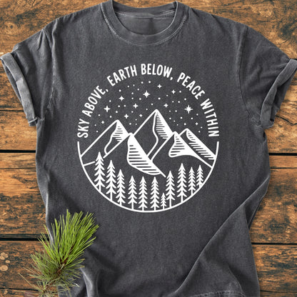 Sky Above - Vintage Wash Tee features a white line-art design of mountains, pine trees, and a starry sky, with the phrase “SKY ABOVE, EARTH BELOW, PEACE WITHIN,” on a dark-gray T-shirt.