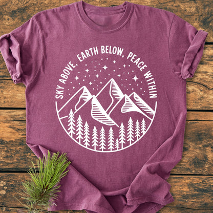 Sky Above - Vintage Wash Tee, featuring a white circular graphic with mountains, pine trees, and stars, laid on wood. The heather-purple tee offers a relaxed fit with durable double-needle stitching.
