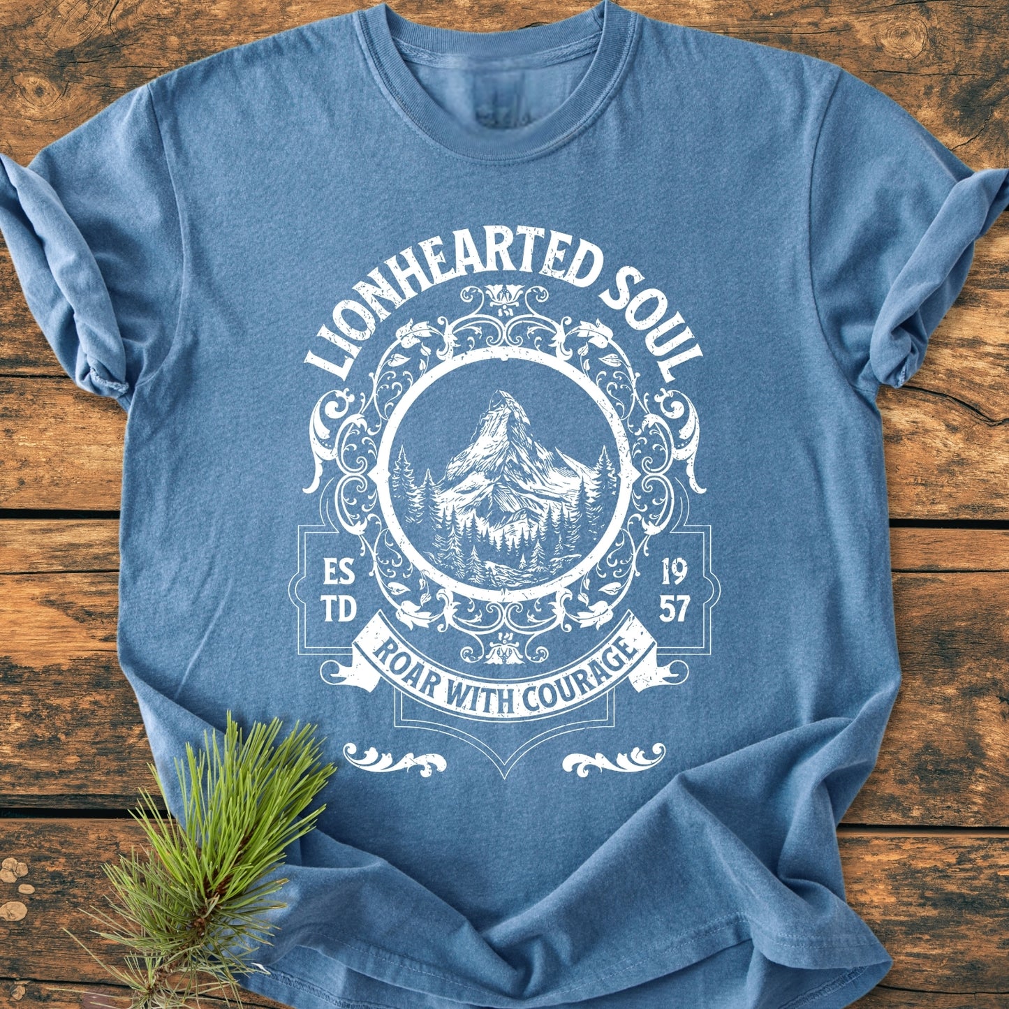 Lionhearted Soul - Vintage Wash Tee featuring a white, vintage-style graphic with LIONHEARTED SOUL, a mountain peak, pine trees, and ROAR WITH COURAGE banner, laid on rustic wood.