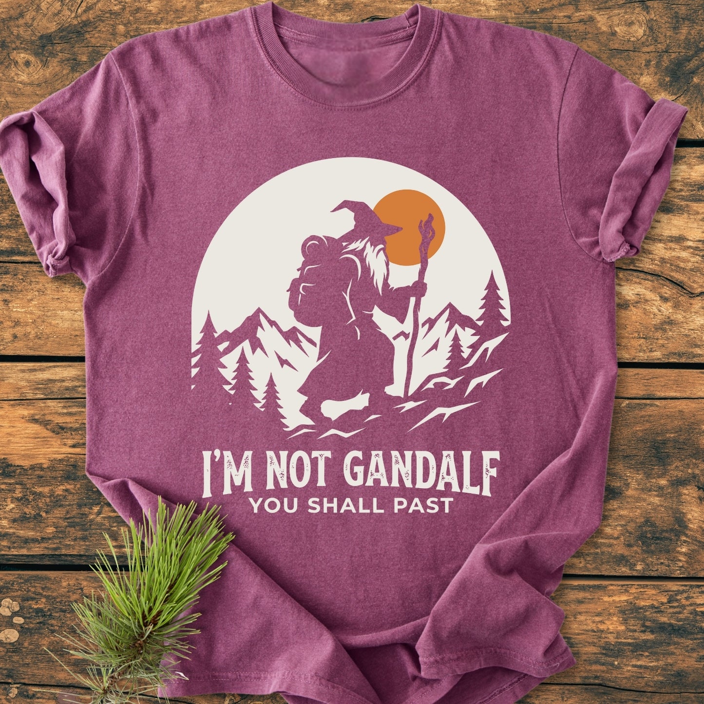 You Shall Past - Vintage Wash Tee features a white wizard graphic with mountains, trees, and sun, complemented by the slogan. Laid on wood, showcasing its relaxed fit and durable craftsmanship.