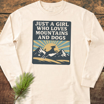 Just A Girl Who Loves Dogs Comfort Colors Long-Sleeve Tee featuring a retro mountain and dog graphic, laid flat with a pine sprig, exemplifying its nature-inspired design and comfort-focused cotton fabric.