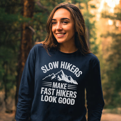Young woman in a forest wearing the Slow Hikers Make Fast Hikers Look Good Long-Sleeve Tee, showcasing a relaxed fit and mountain graphic, perfect for casual, comfortable outings.