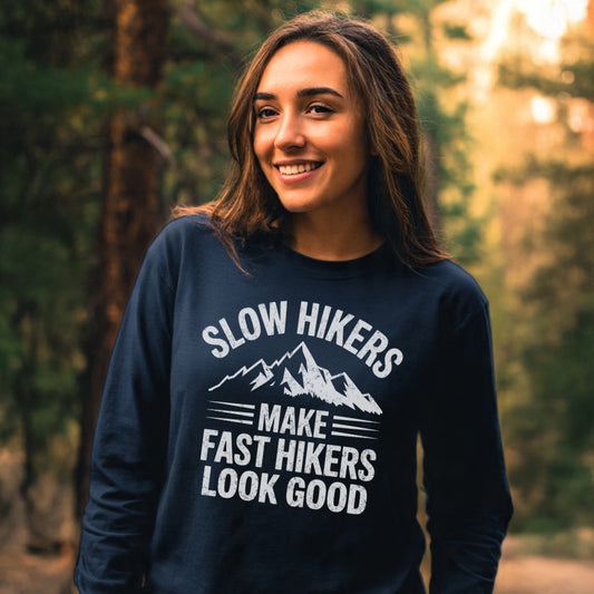 Young woman in a forest wearing the Slow Hikers Make Fast Hikers Look Good Long-Sleeve Tee, showcasing a relaxed fit and mountain graphic, perfect for casual, comfortable outings.