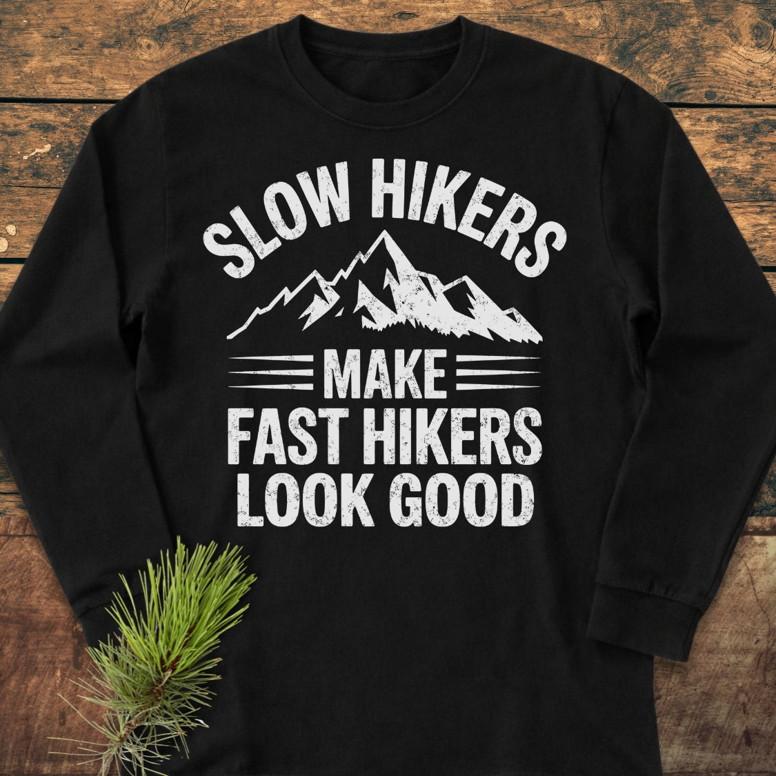 Slow Hikers Make Fast Hikers Look Good Long-Sleeve Tee displayed on wood, featuring white mountain peaks graphic and bold text. Made from 100% ring-spun cotton with a relaxed fit for comfort.