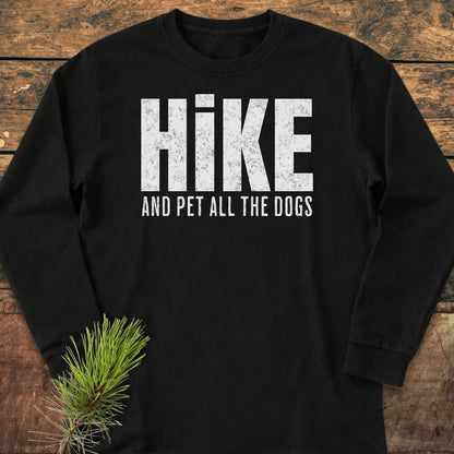 Hike And Pet Dogs Long-Sleeve Tee, black with distressed white lettering, laid on wood. Made of 100% ring-spun cotton, it offers a classic fit and soft, casual style.