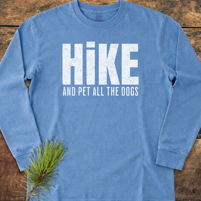 Sky-blue Hike And Pet Dogs Long-Sleeve Tee on a wooden surface, featuring distressed white text. A pine sprig accents the shirt, highlighting its casual, comfortable design.