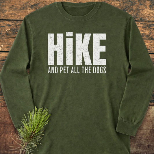 Hike And Pet Dogs Long-Sleeve Tee on rustic wood, featuring bold white text and a pine branch. Made from soft, 100% ring-spun cotton, this garment-dyed tee offers a relaxed fit.