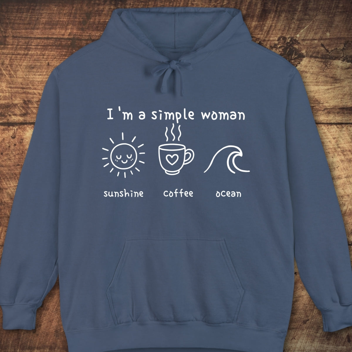 I'm A Simple Woman - Sunshine Coffee Ocean Hoodie, featuring a white hand-drawn graphic on the chest, laid flat against a wooden background, showcasing its relaxed, cozy design ideal for layering.
