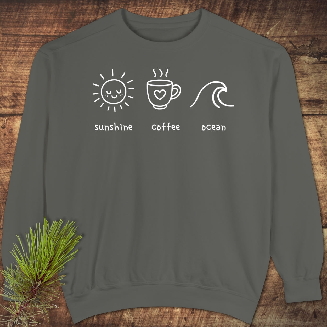 I'm A Simple Woman - Sunshine Coffee Ocean Sweatshirt on wooden surface, featuring white icons: a smiling sun, a coffee cup with heart, and an ocean wave, embodying comfort and style.