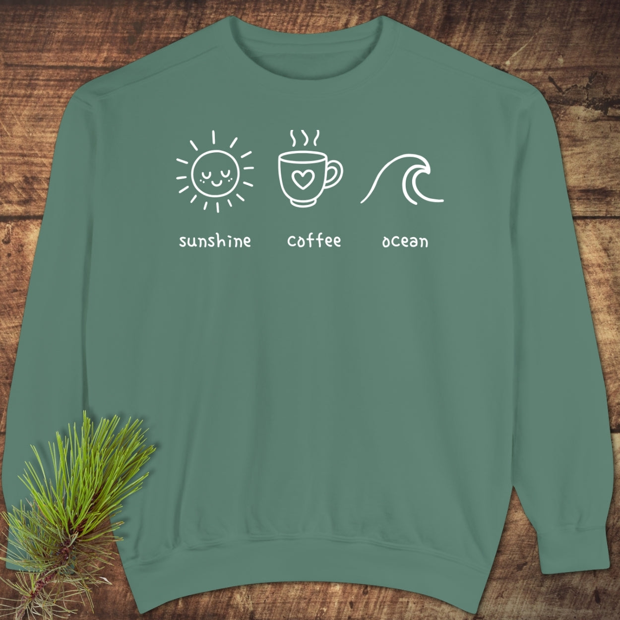 I'm A Simple Woman - Sunshine Coffee Ocean Sweatshirt, featuring a teal design with white sun, coffee, and wave illustrations, shown on a wood background with a pine sprig accent.