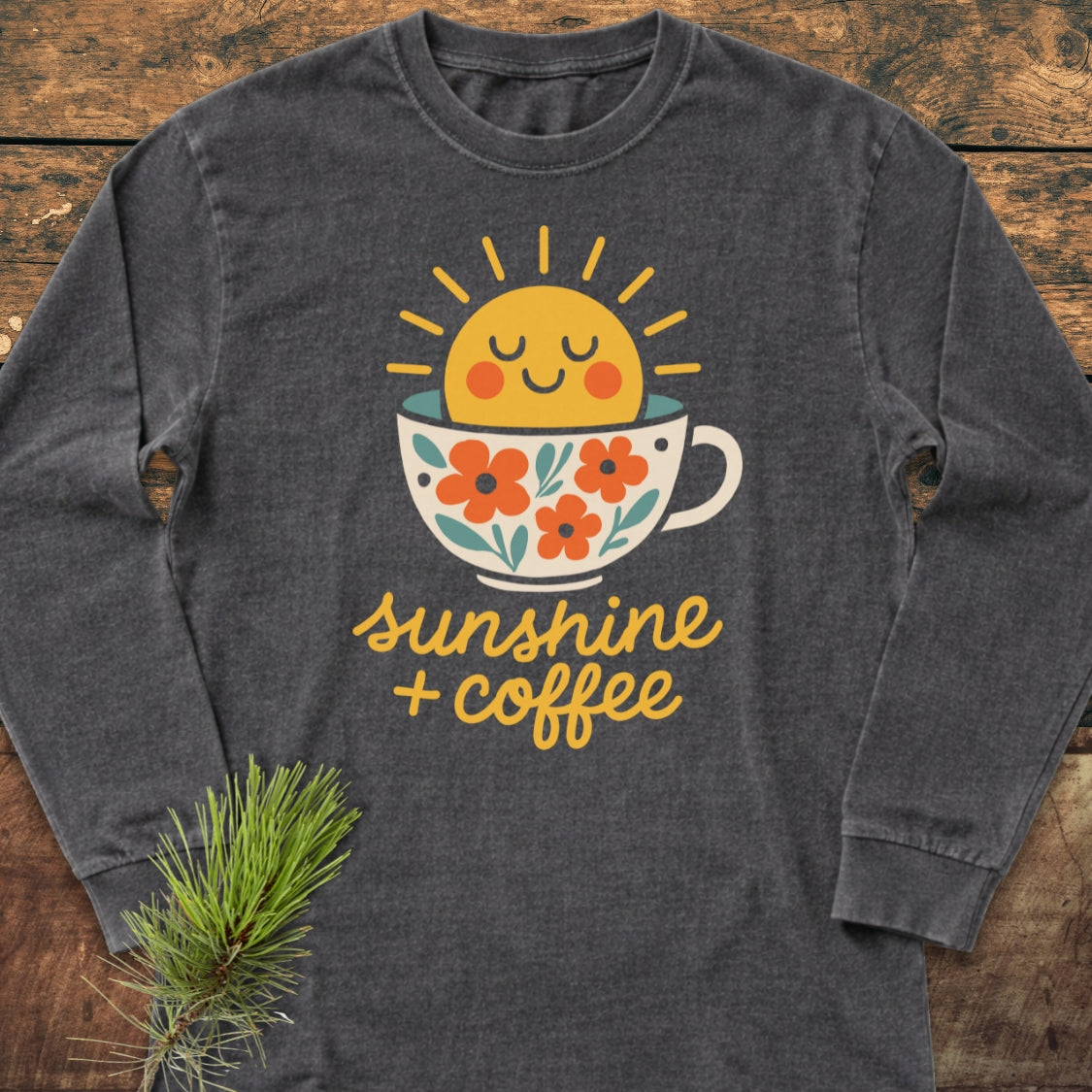 Sunshine And Coffee Long-Sleeve Tee features a smiling sun graphic emerging from a floral coffee cup with sunshine + coffee text, showcasing its whimsical design on dark-gray fabric.