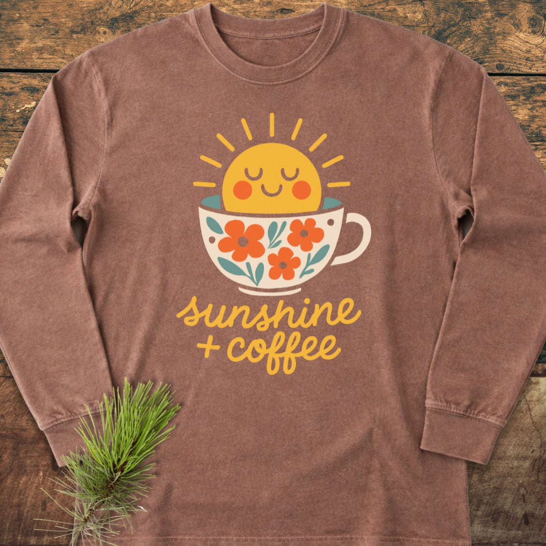Sunshine And Coffee Long-Sleeve Tee featuring a smiling sun in a coffee cup with flowers, laid on wood. Made of 100% ring-spun cotton, offering a classic fit and casual comfort.