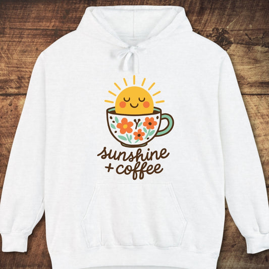 Sunshine And Coffee Hoodie with a colorful sun and coffee cup graphic, featuring sunshine + coffee text. Laid on wood surface, showcasing its cozy, garment-dyed fabric and relaxed unisex fit.