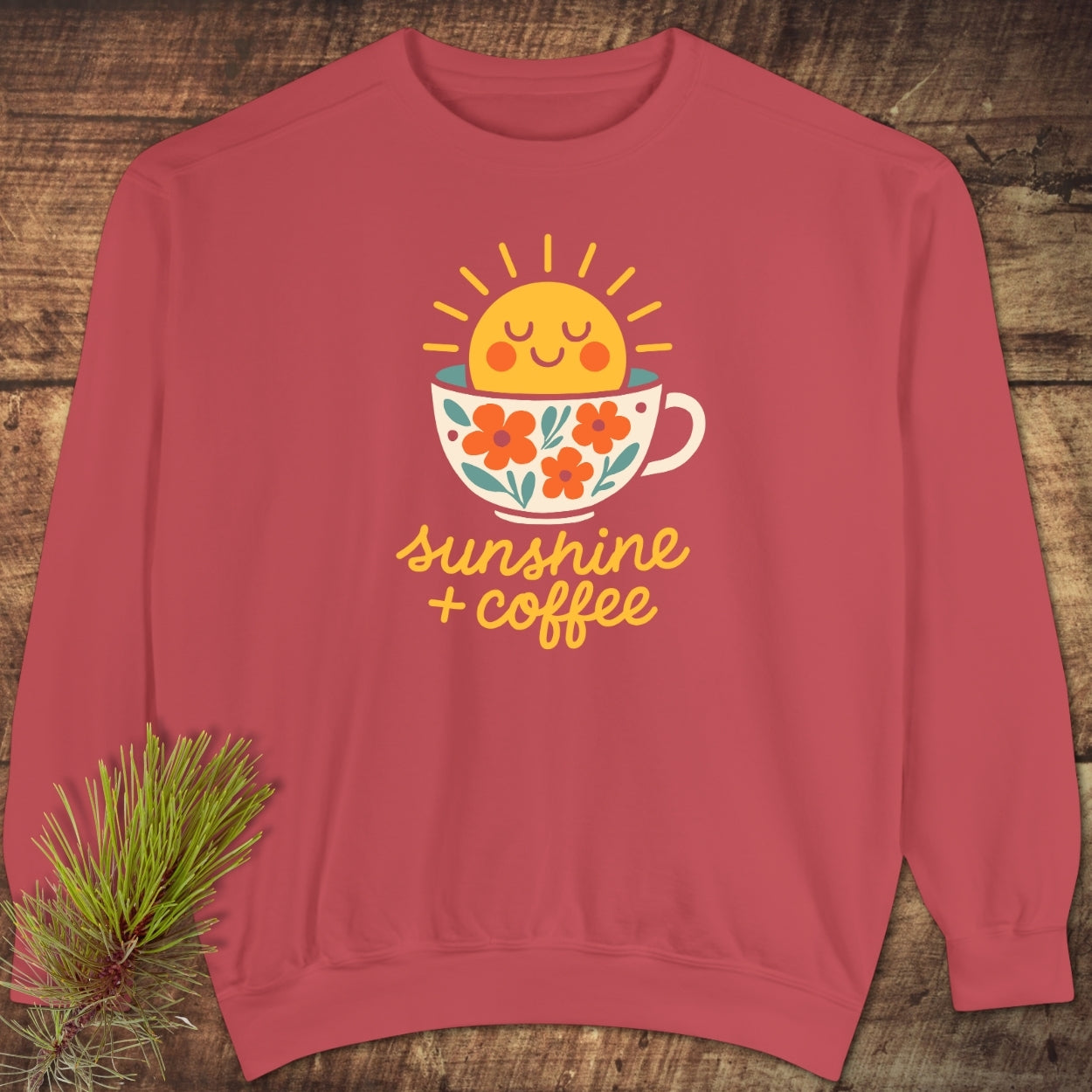 Sunshine And Coffee Sweatshirt features a smiling sun in a teacup graphic, laid on a wooden surface. This unisex, relaxed-fit, crew-neck top is crafted from garment-dyed, ring-spun cotton-polyester blend.