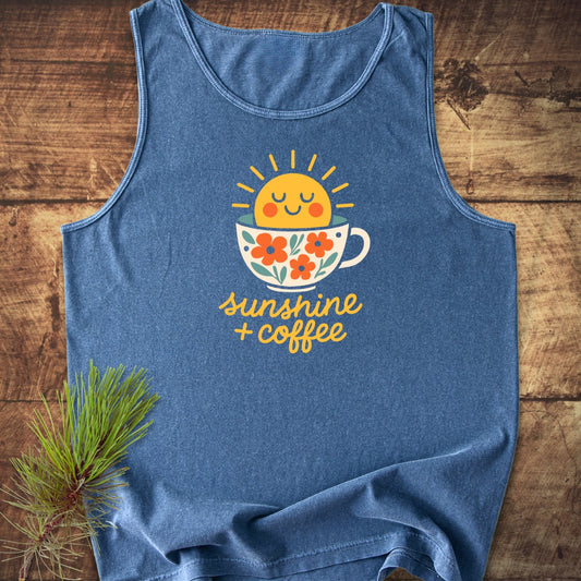Sunshine And Coffee Tank Top featuring a cheerful sun in a floral coffee cup graphic, laid on wood with a pine branch. Made from 100% US cotton for comfort and sustainability.