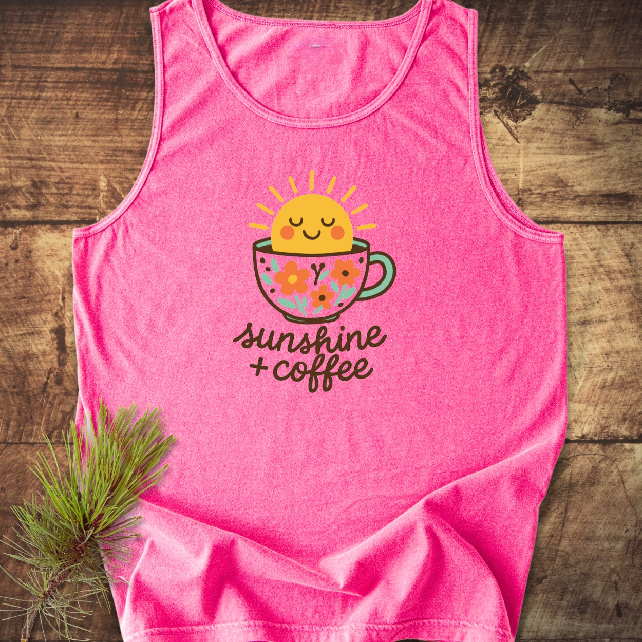 Sunshine And Coffee Tank Top featuring a cartoon coffee cup with a smiling sun and flowers, laid on rustic wood. Made of 100% US cotton, emphasizing comfort, sustainability, and playful design.