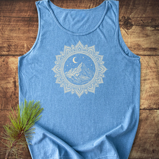 Mountain Mandala Tank Top in heather-blue, featuring a cream mandala graphic of a mountain under a crescent moon, laid on wood with a pine branch accent.