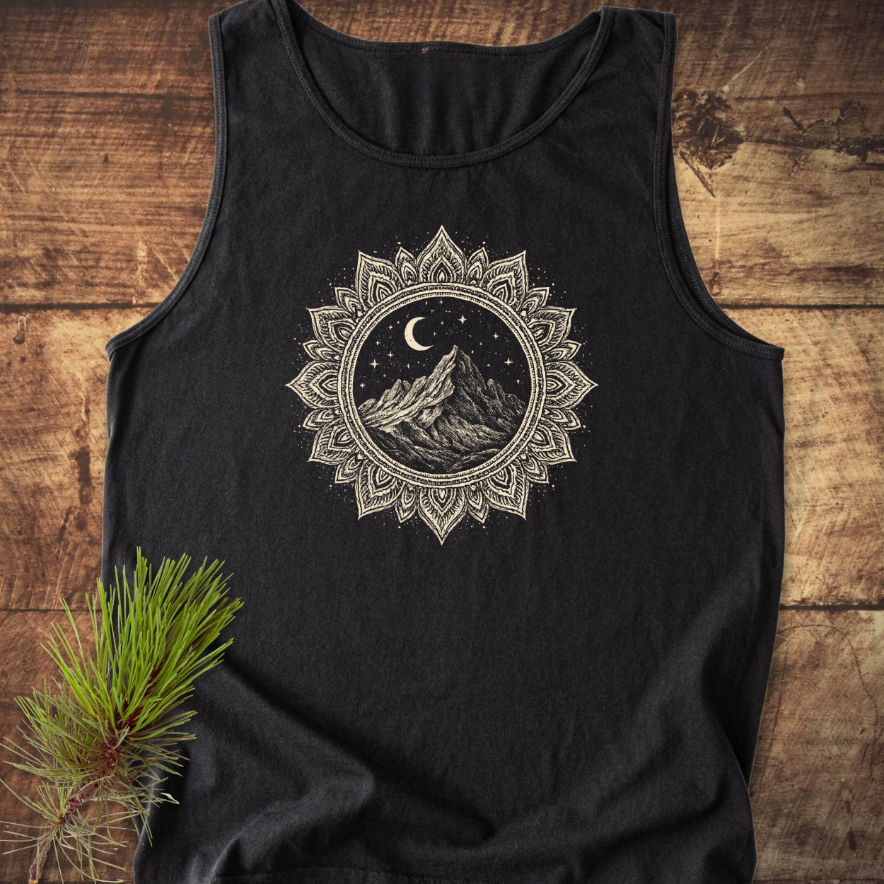 Mountain Mandala Tank Top on rustic wood, featuring a cream mandala graphic with a mountain, crescent moon, and stars, exemplifying its relaxed fit, ethical production, and sustainable material.