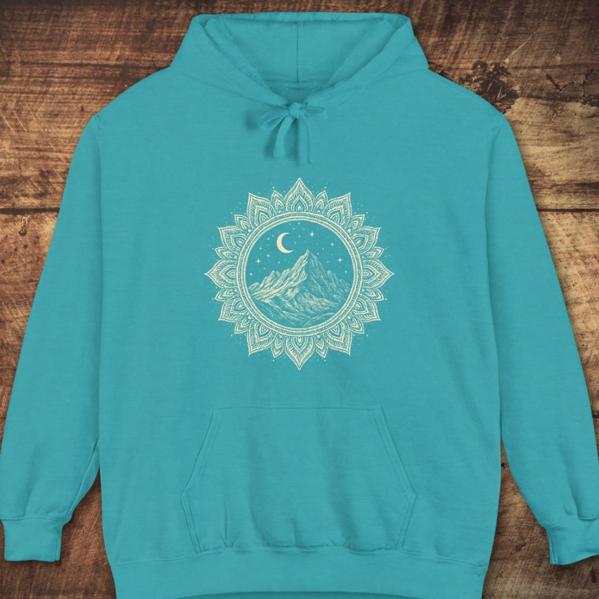 Mountain Mandala Hoodie features a stylized mountain design under a crescent moon and stars within a mandala border on a teal sweatshirt, complete with a kangaroo pocket and drawstring hood.