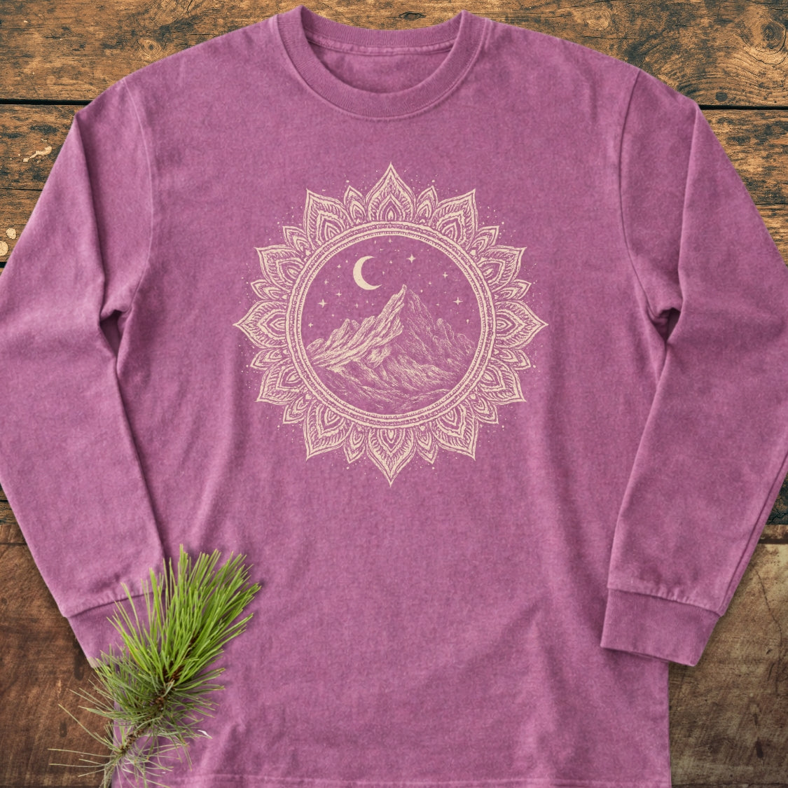 Mountain Mandala Long-Sleeve Tee featuring a heathered purple design with a cream mandala mountain graphic under a crescent moon, laid flat on wood, accented by a pine twig.