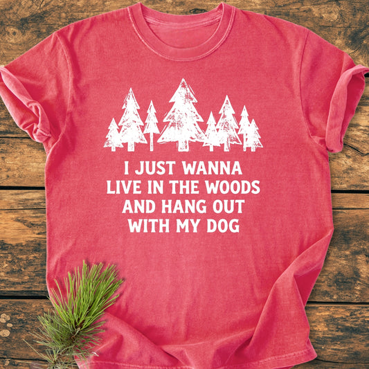 Live In The Woods - Vintage Wash Tee features a white pine tree graphic and slogan on a red-coral shirt, laid flat on wood, with a pine sprig beside it.