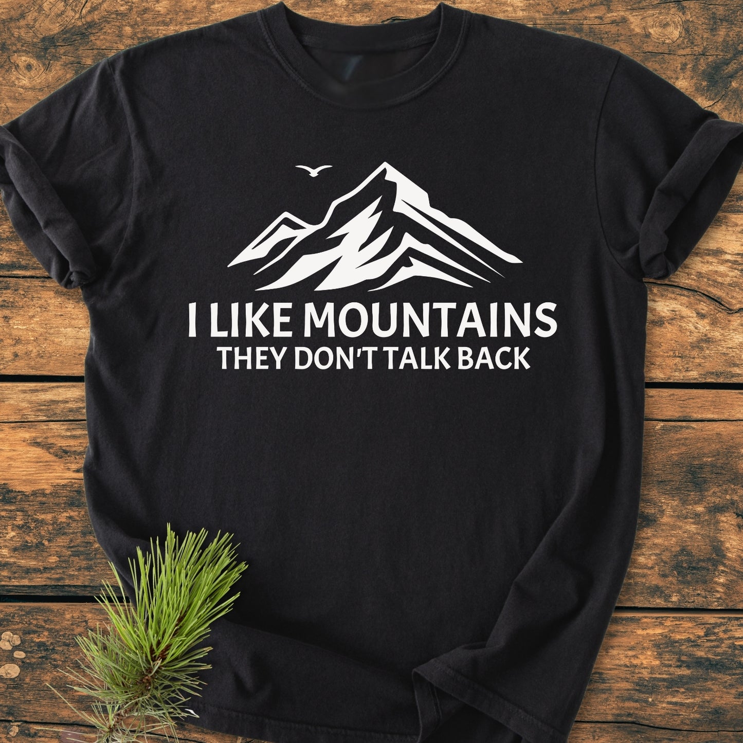 I Like Mountains - Vintage Wash Tee featuring a mountain silhouette and slogan, laid on wood with a pine sprig, showcases a relaxed fit and durable stitching for everyday comfort.