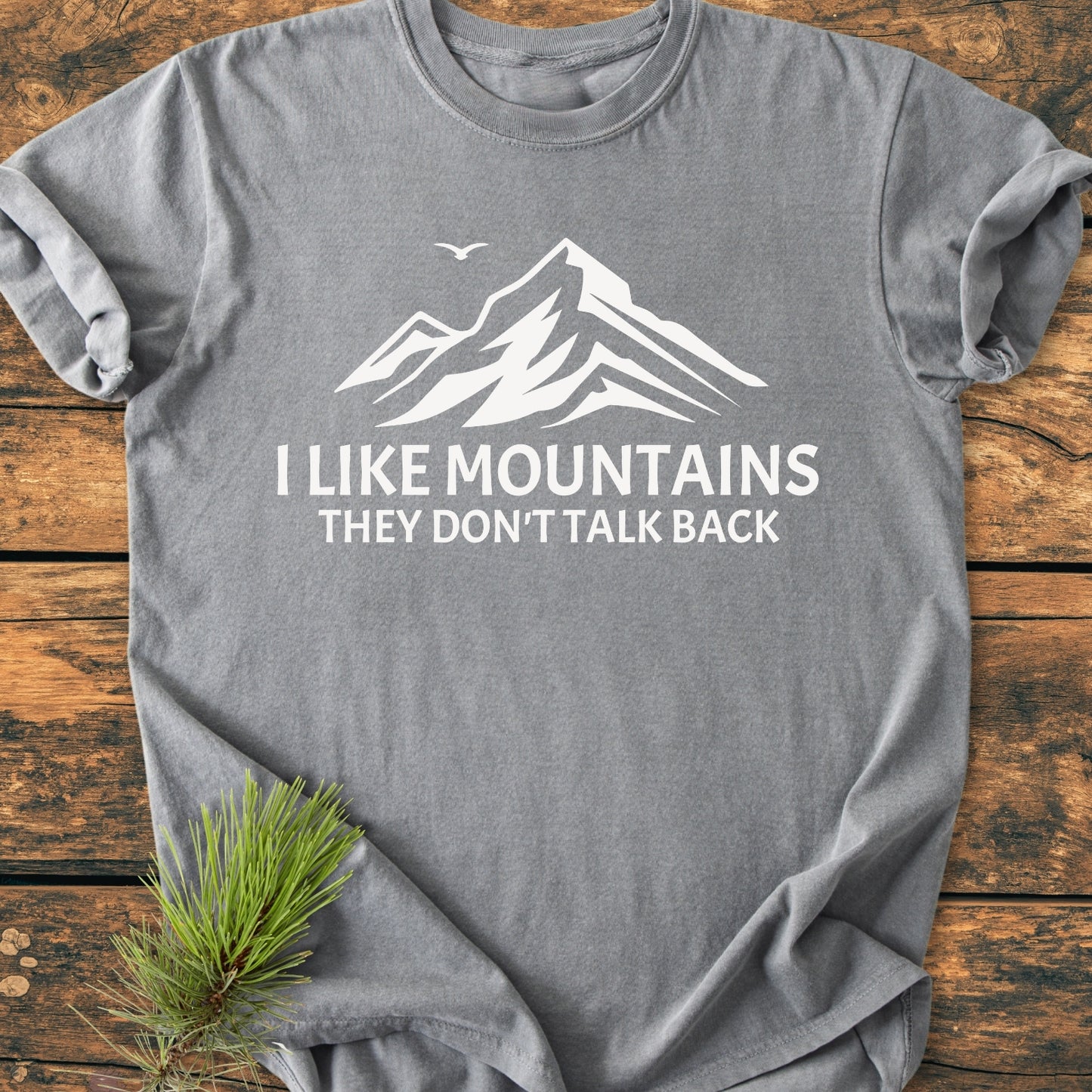 Heather-gray I Like Mountains - Vintage Wash Tee with white mountain graphic and slogan, laid flat on wood. Includes a pine branch accent. Made of soft, pre-shrunk, ring-spun cotton.