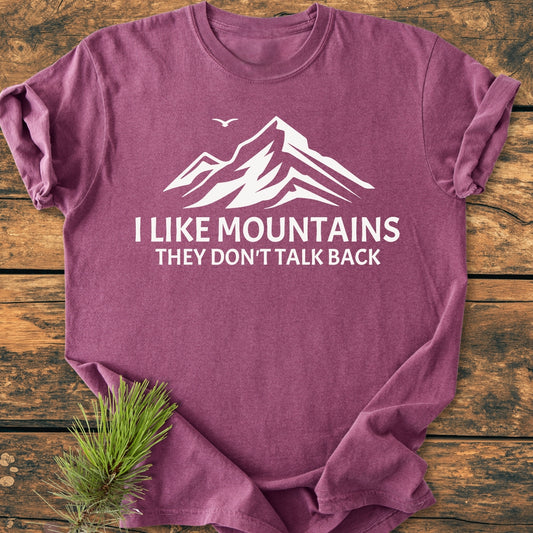 Heather-purple I Like Mountains - Vintage Wash Tee with a white mountain graphic and slogan, laid flat on wood with an evergreen sprig, showcasing its relaxed fit and durable stitching.