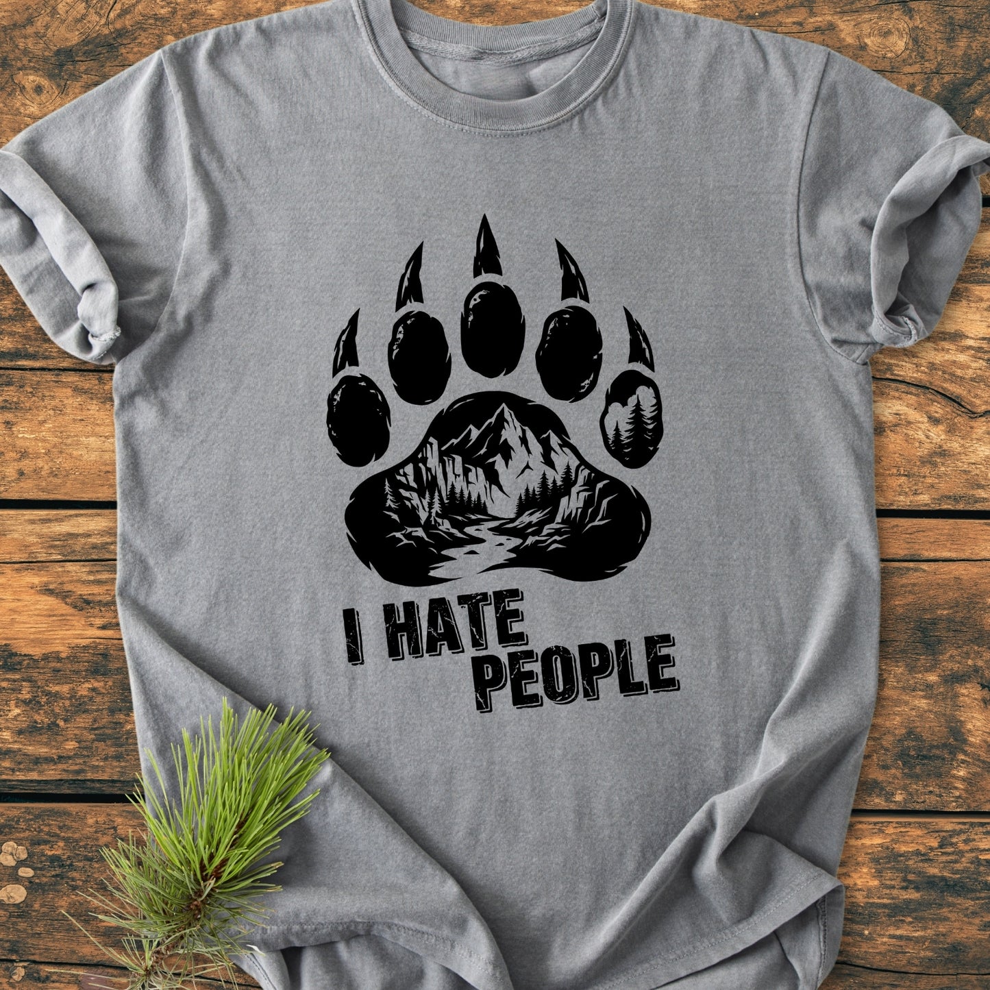 Heather-gray I Hate People - Vintage Wash Tee featuring a black bear-paw graphic with mountain-forest design, bold slogan, and rustic pine branch, showcasing a relaxed fit on a wooden surface.