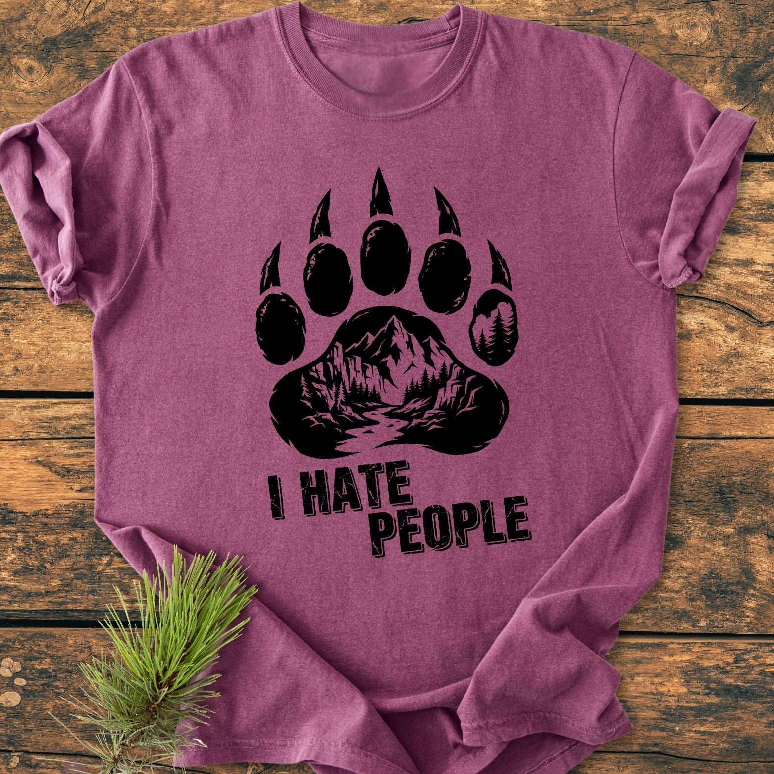Purple I Hate People - Vintage Wash Tee featuring a black stylized bear paw with a mountain-and-forest scene, laid on a wooden surface; perfect for a cozy, relaxed daily wear.