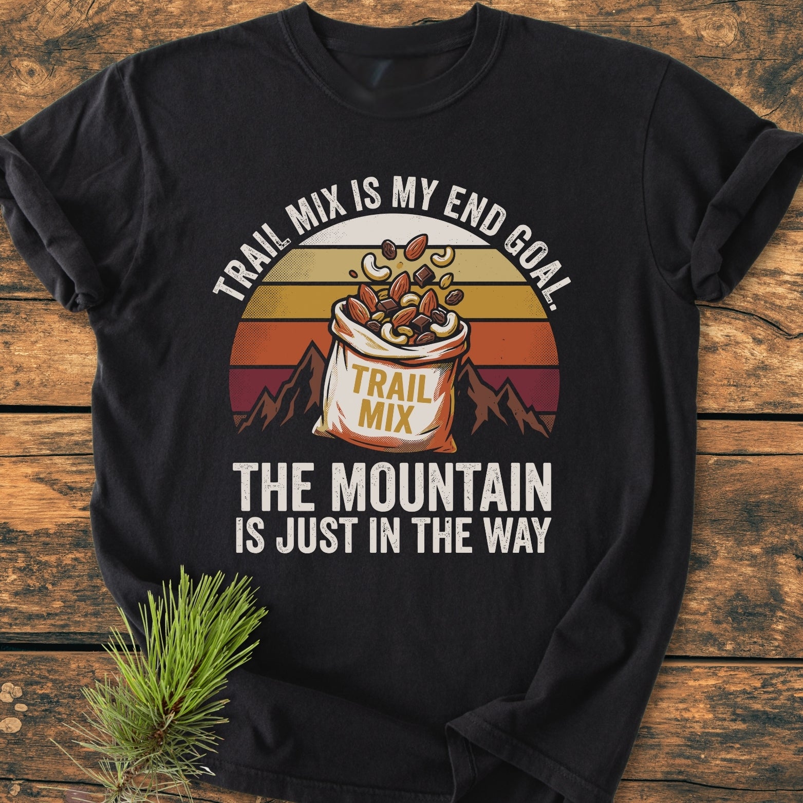 Trail Mix End Goal - Vintage Wash Tee featuring a retro graphic of trail mix against a sunset and mountains, laid on wood with a pine branch; soft-washed, relaxed fit, 100% cotton.