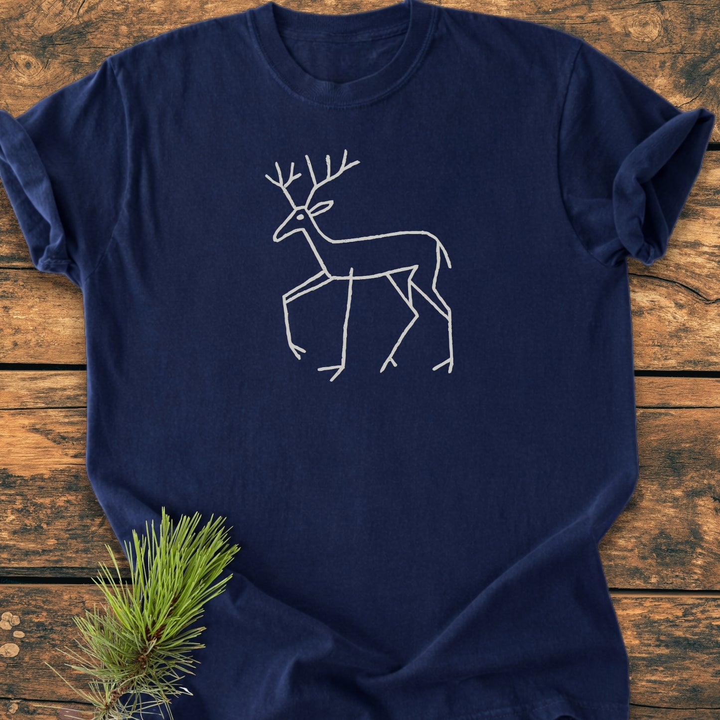 Deer Tribal - Vintage Wash Tee, a navy-blue shirt with a white deer line-drawing, displayed on wood. Features garment-dyed, soft-washed cotton for comfort and durability, ideal for daily wear.